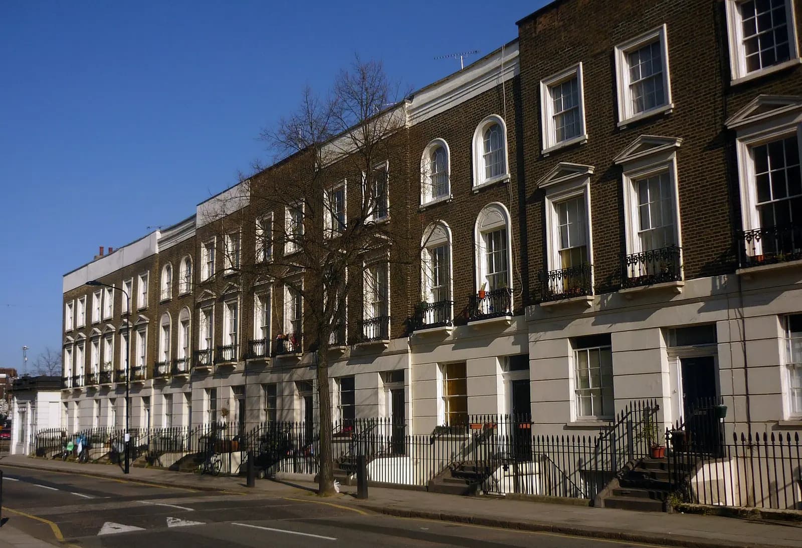 A long Georgian terrace of dark brick houses with arched windows and black railings on Calthorpe Street in Camden, a bare tree on the pavement