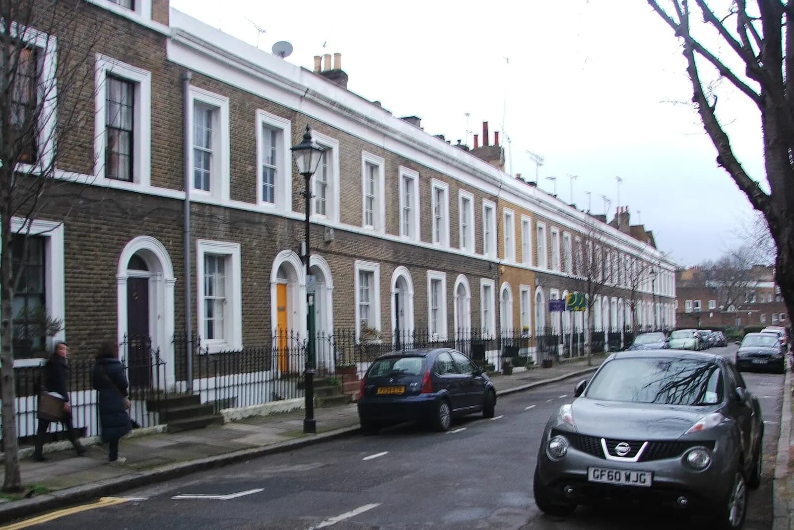 A curving Georgian terrace of brown brick houses with white arched doorways and window surrounds on Remington Street in Islington, a lamp post and parked cars