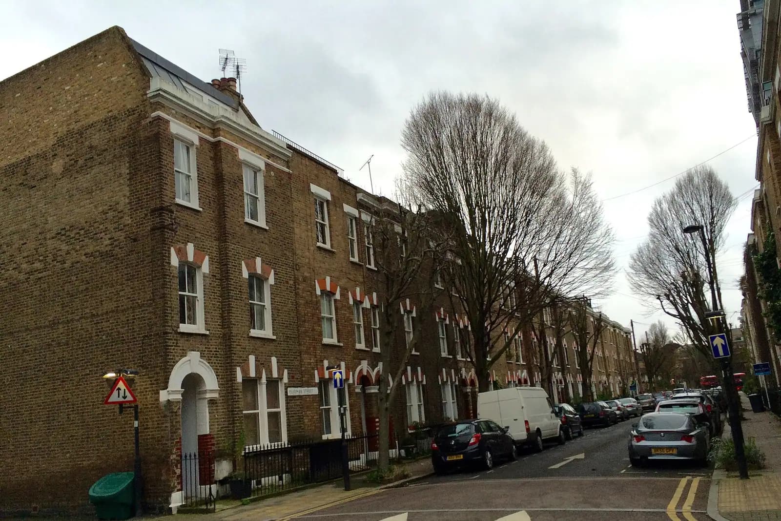 A corner of yellow-brick Victorian terraced houses with red brick arches over the windows on Pearman Street in Lambeth, a white van and bare trees