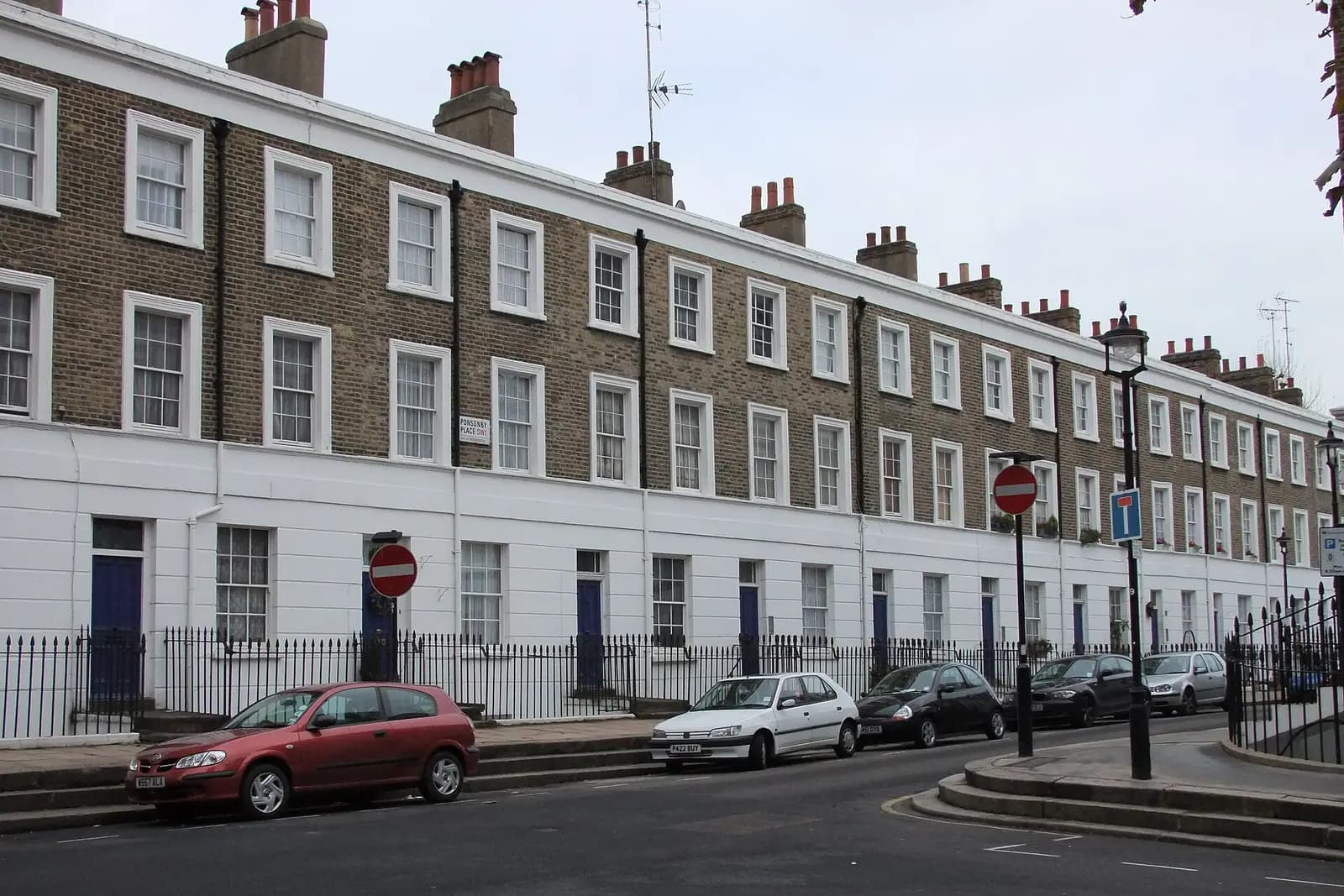 A long terrace of brown brick houses above a white stuccoed ground floor on Ponsonby Place in Westminster, with iron railings and no-entry signs
