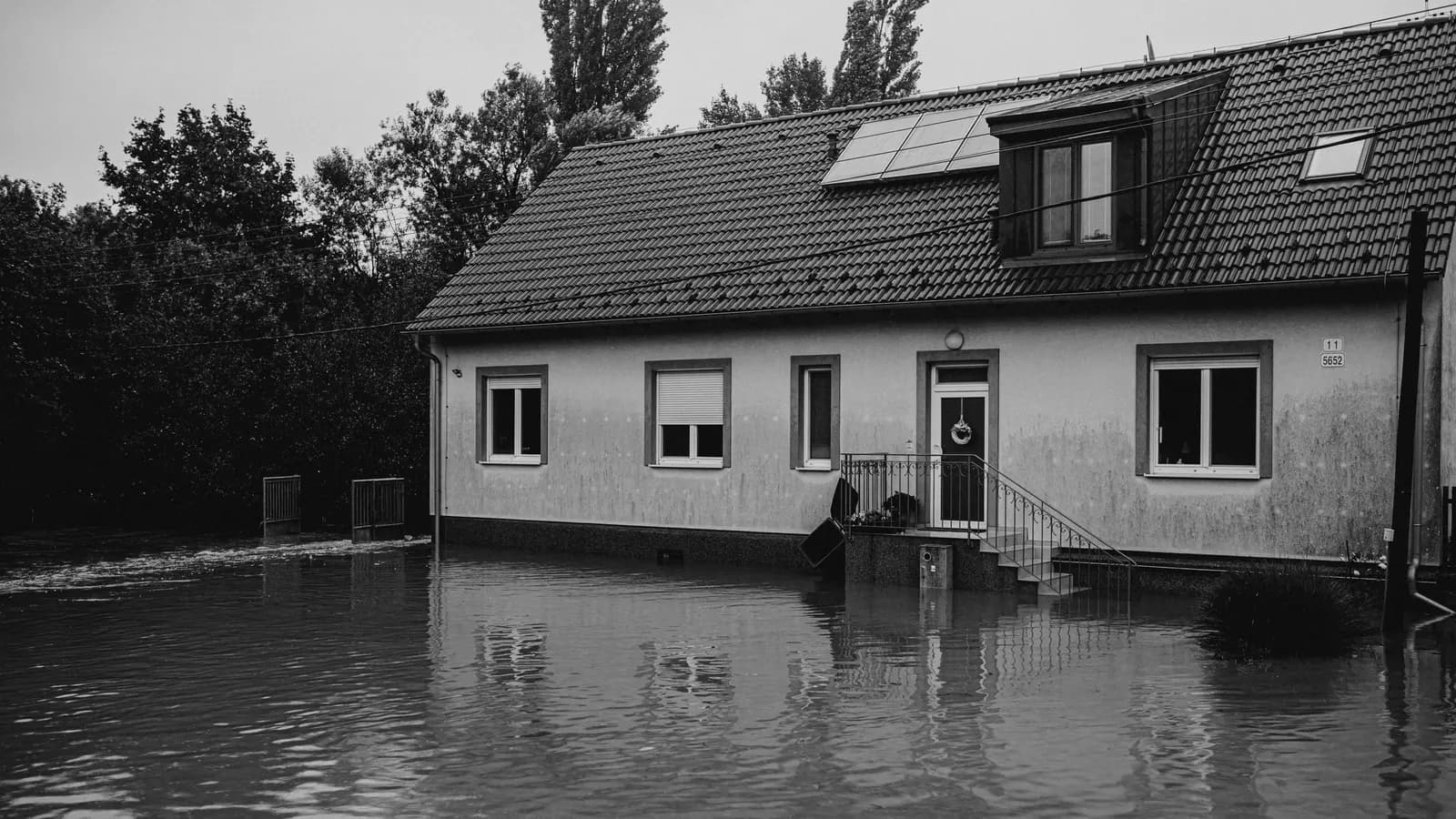 A black-and-white view of a tiled-roof house with a front door and steps, surrounded by floodwater
