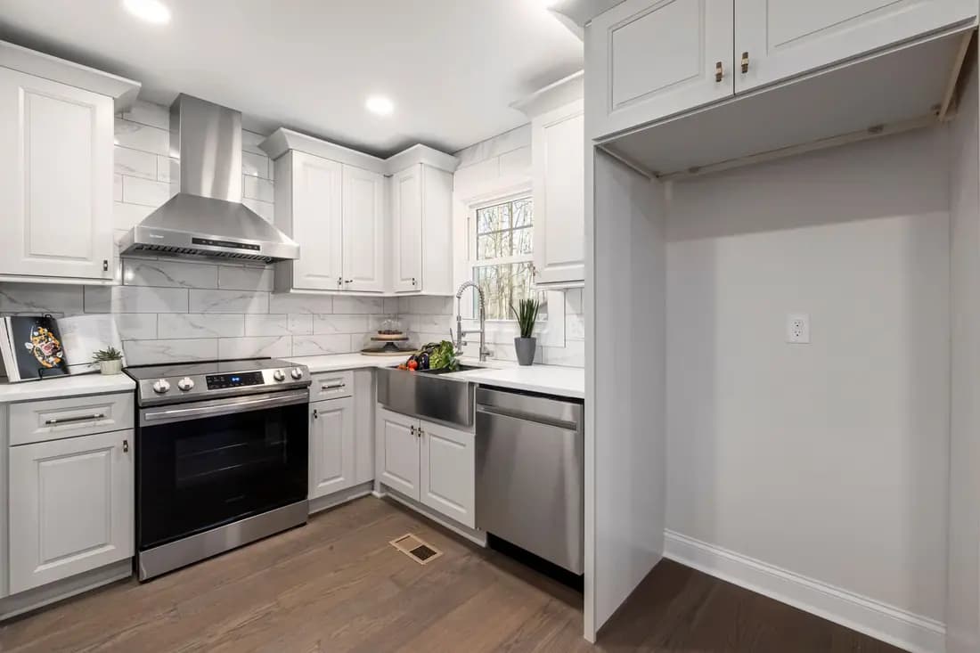 A bright kitchen with white cabinets, a stainless steel range cooker and extractor hood, and a window over the sink