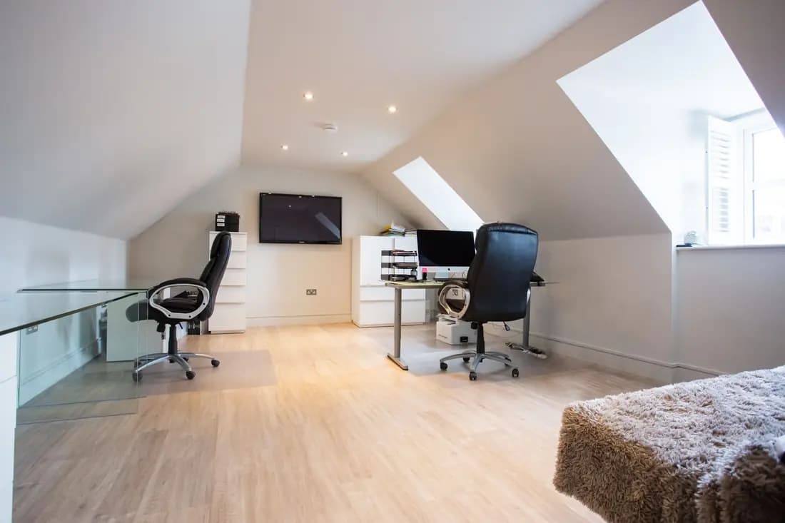 A finished loft room with a sloping ceiling, two roof windows and a light wood floor