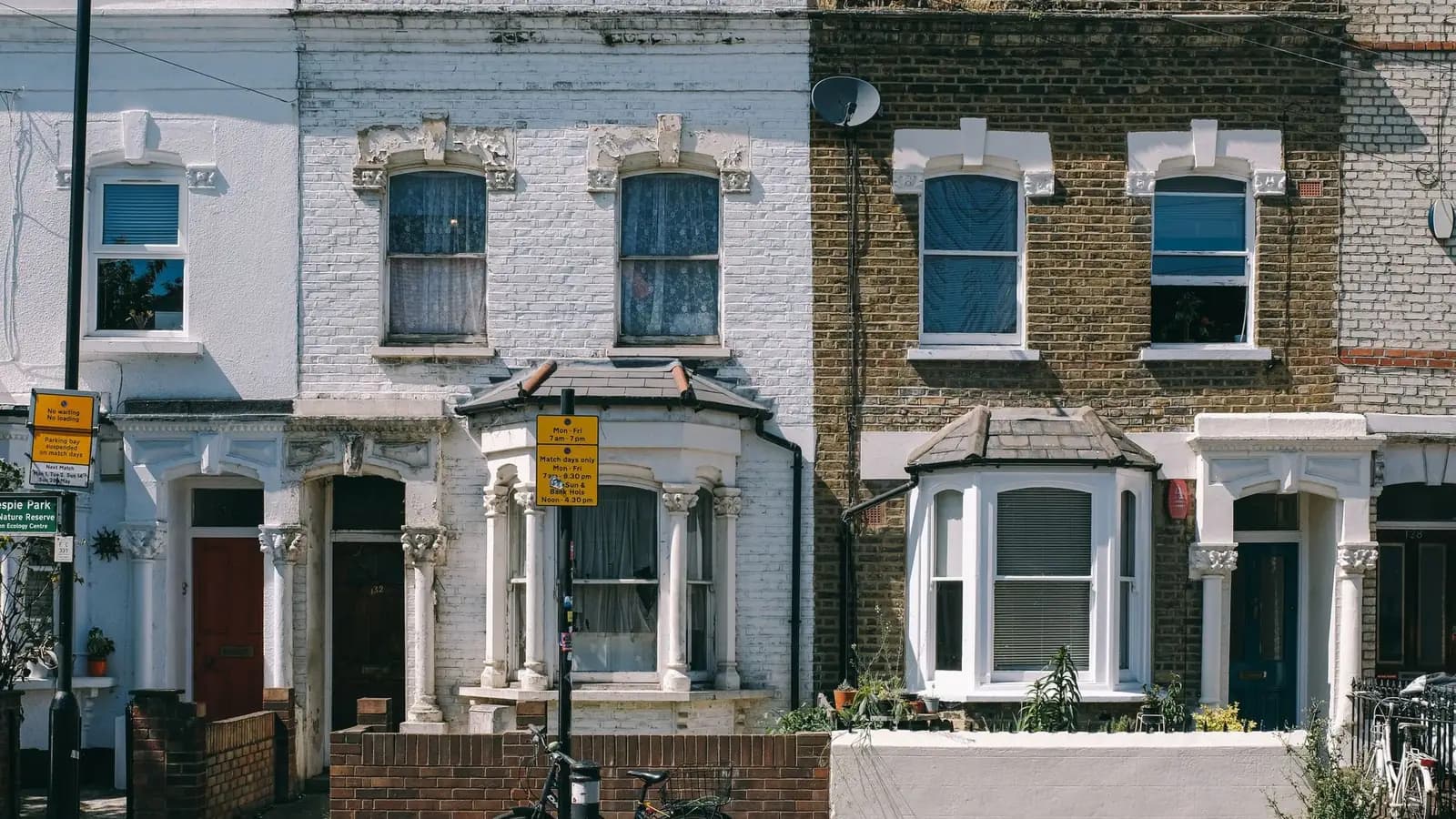 Two Victorian terraced houses on a London street, one painted white and one in yellow stock brick, with bay windows