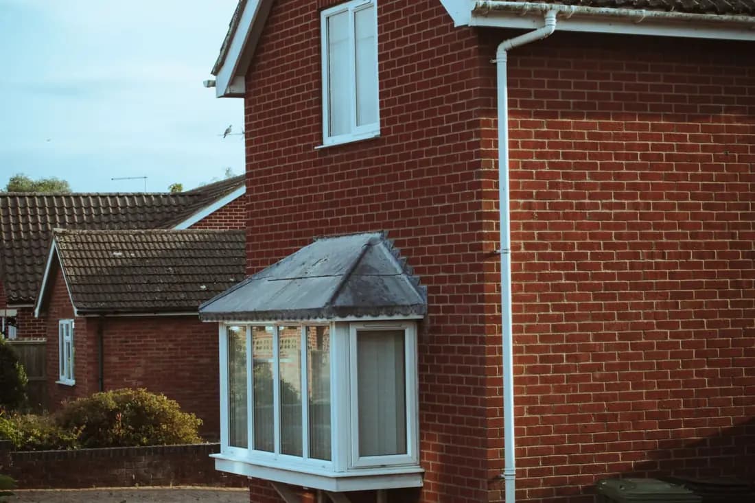 The side and front of a red brick house with a white bay window