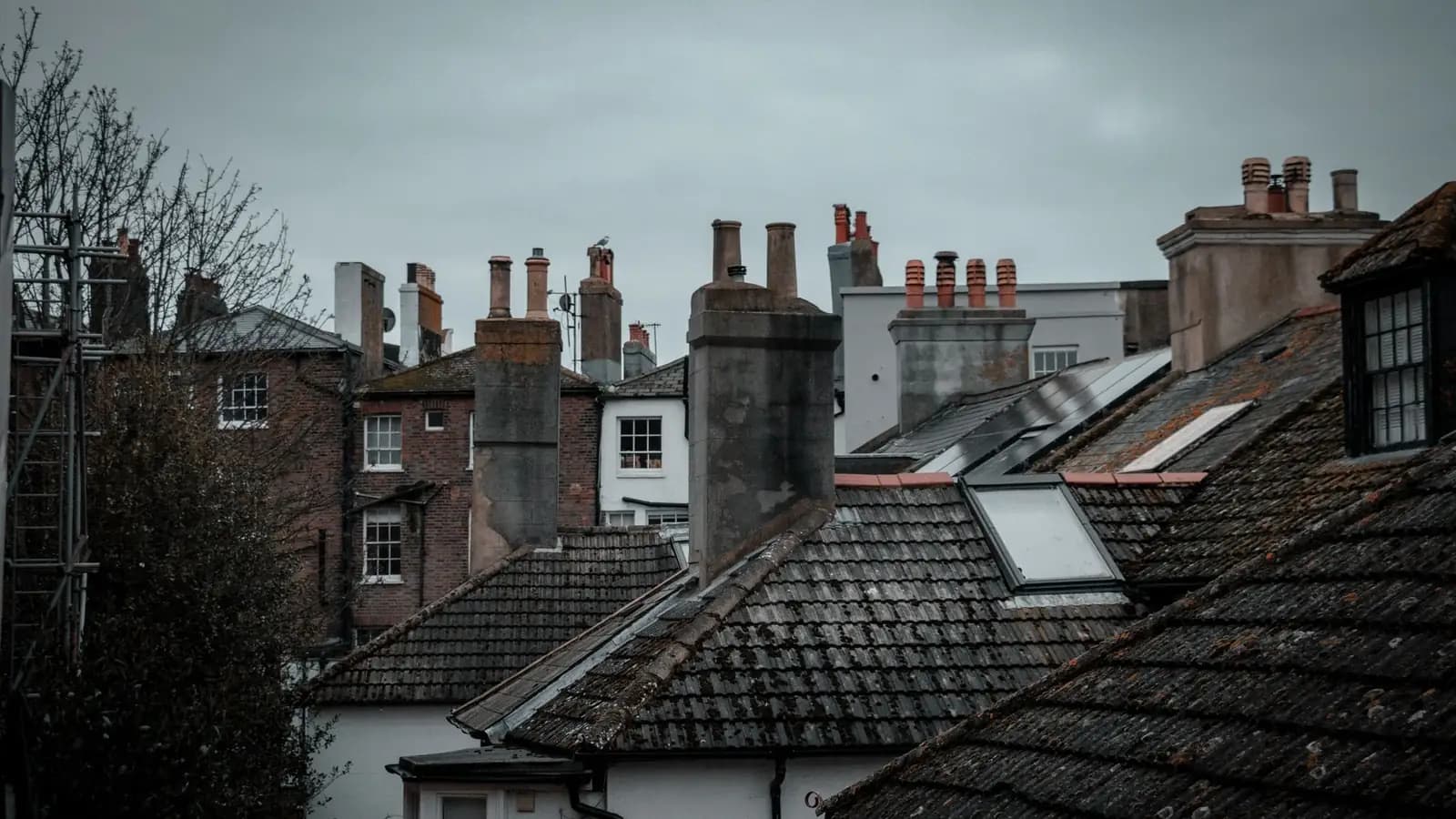 Tiled roofs, chimney stacks and roof windows on a row of older English houses under a grey sky