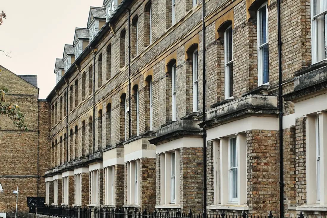 A long row of Victorian brick terraced houses with sash windows seen along the pavement