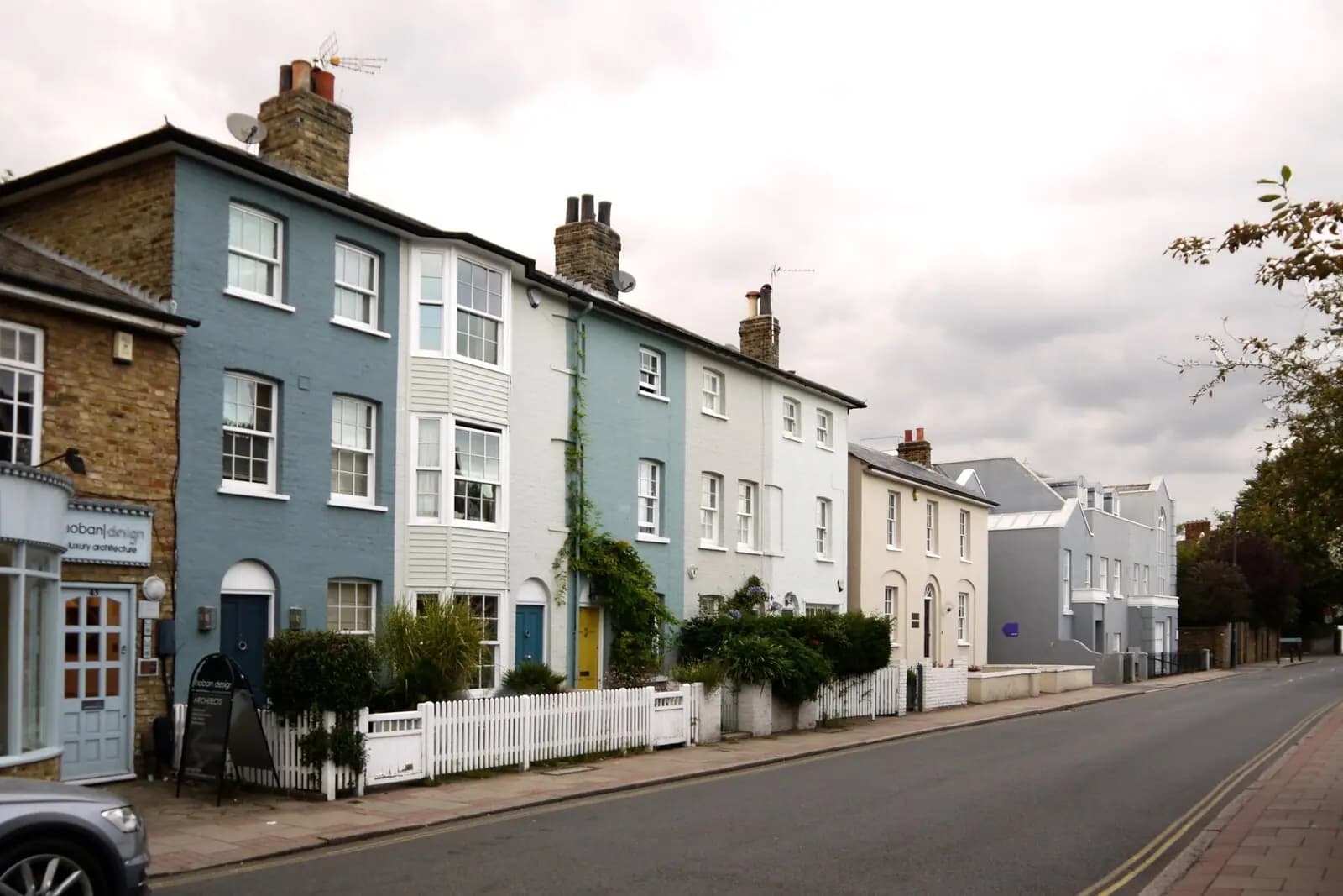A row of painted cottages in blue, white and cream with white sash windows and a picket fence on Church Road in Wimbledon