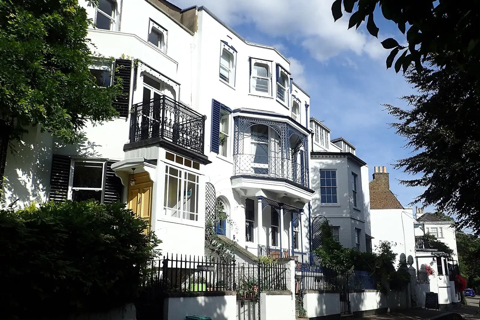 Cream and white Georgian and Victorian houses at Twickenham Riverside with iron balconies, a blue lattice veranda and sunlit trees