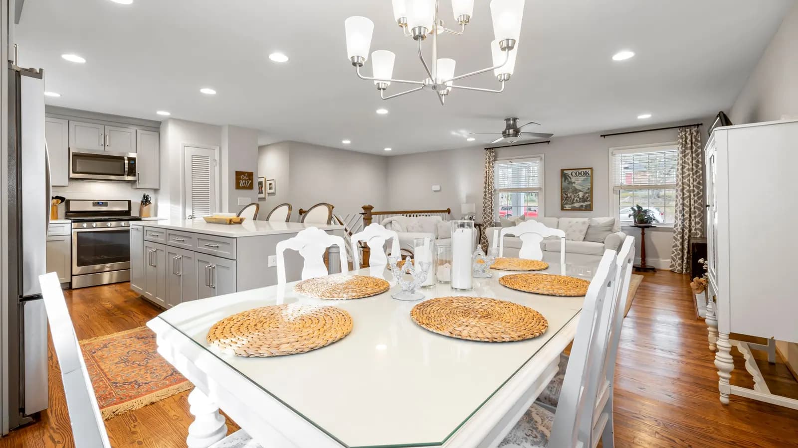 An open-plan kitchen, dining table and sitting area under a chandelier, with grey units and a wood floor