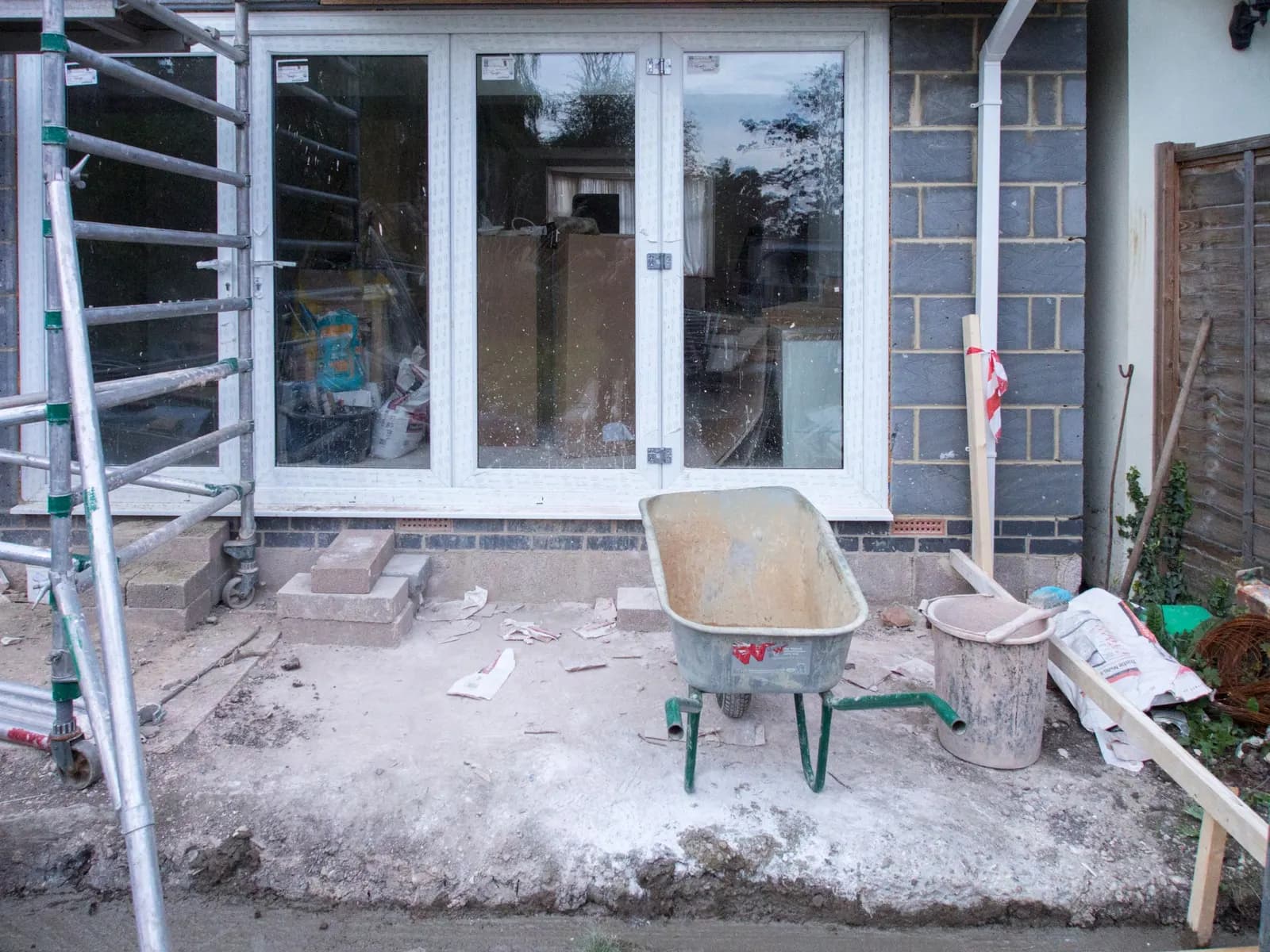 A new single-storey rear extension at shell stage: blockwork walls, white bifold doors, a scaffold tower and a wheelbarrow on the slab
