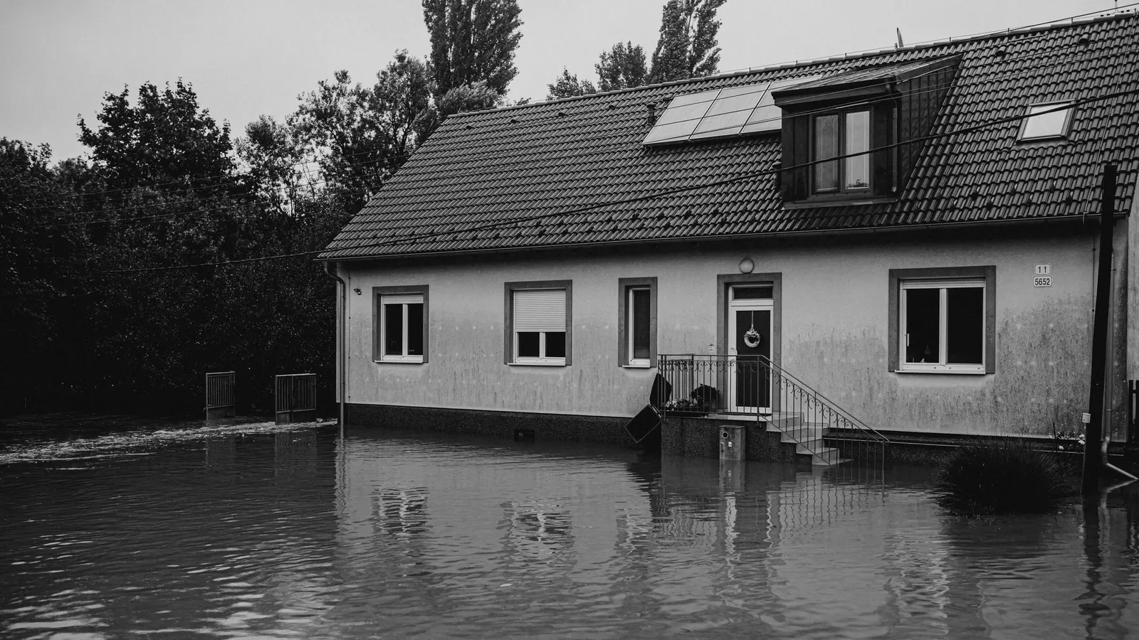 A black-and-white view of a tiled-roof house with a front door and steps, surrounded by floodwater