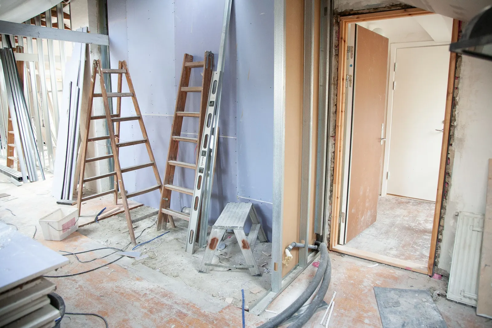 The inside of a house mid-renovation with timber stepladders, metal stud partitions, plasterboard, a spirit level and a new door frame
