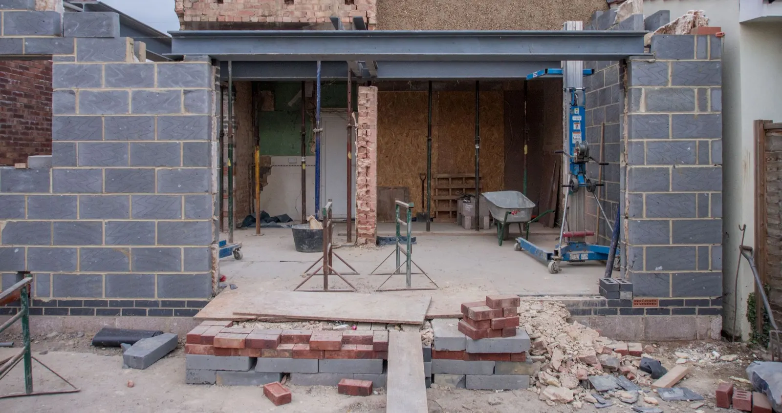 The back of a brick house with a single-storey rear extension under construction, a steel beam spanning the new opening and blockwork walls either side