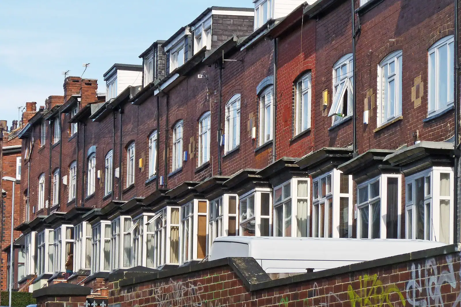 A terrace of red-brick houses stepping up a slope, with bay windows and roof dormers along the front