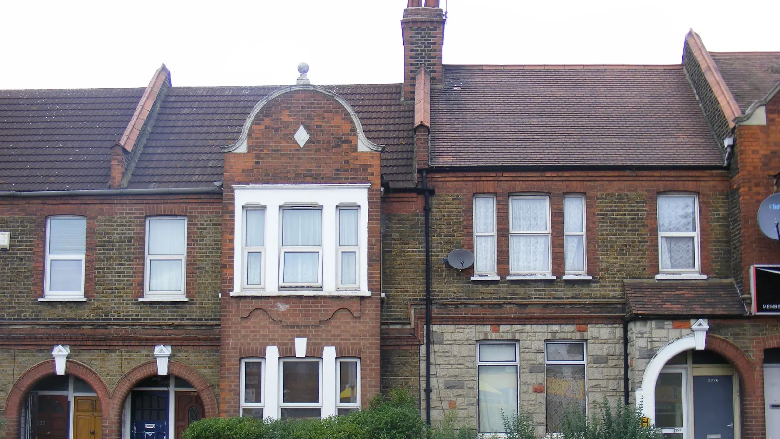 Two storeys of an Edwardian brick terrace in east London, with a white-framed bay window and a curved gable over the middle house