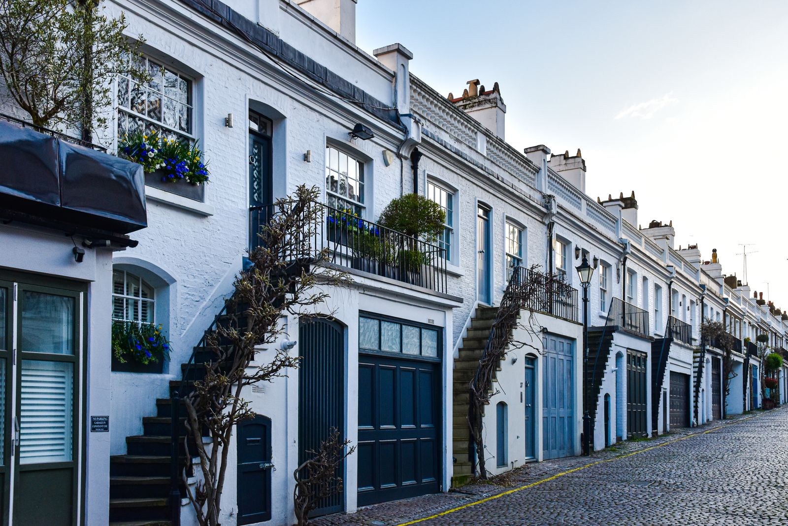 A row of white-painted mews houses with blue doors on a cobbled London street